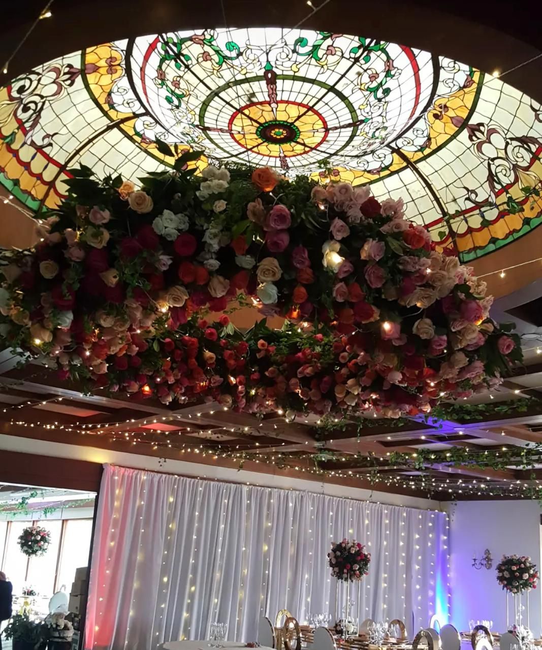 Lámpara floral de rosas bajo un domo de vitral en un salón de bodas