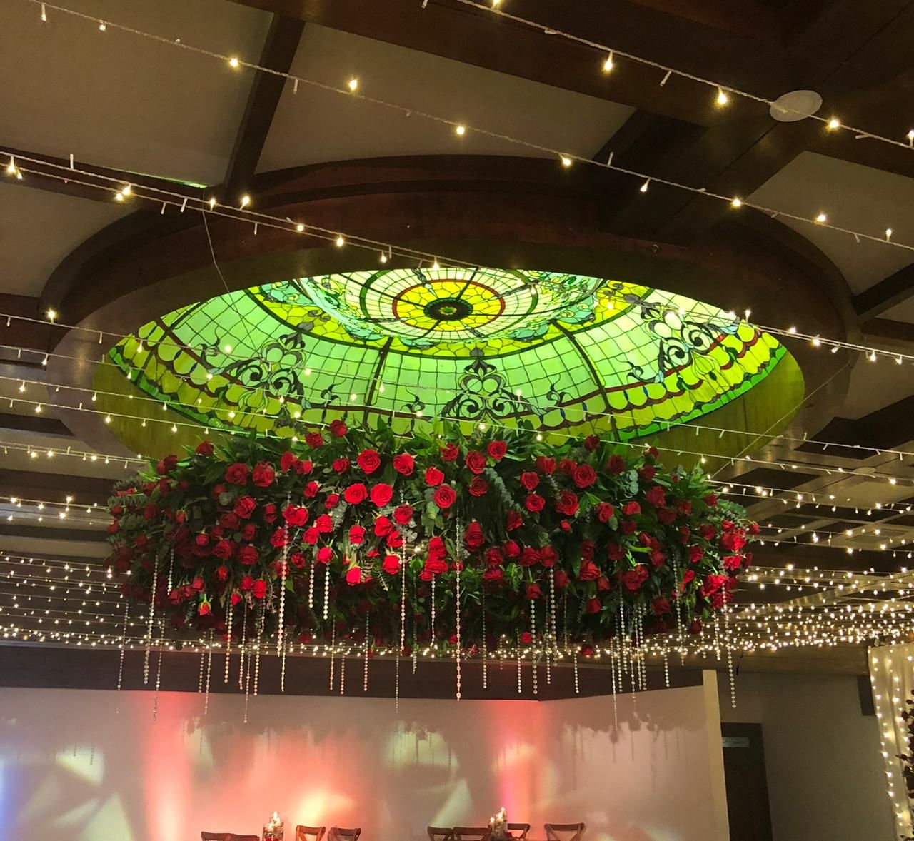 Salón de club con domo de vitral, lámpara de rosas rojas y montaje de boda