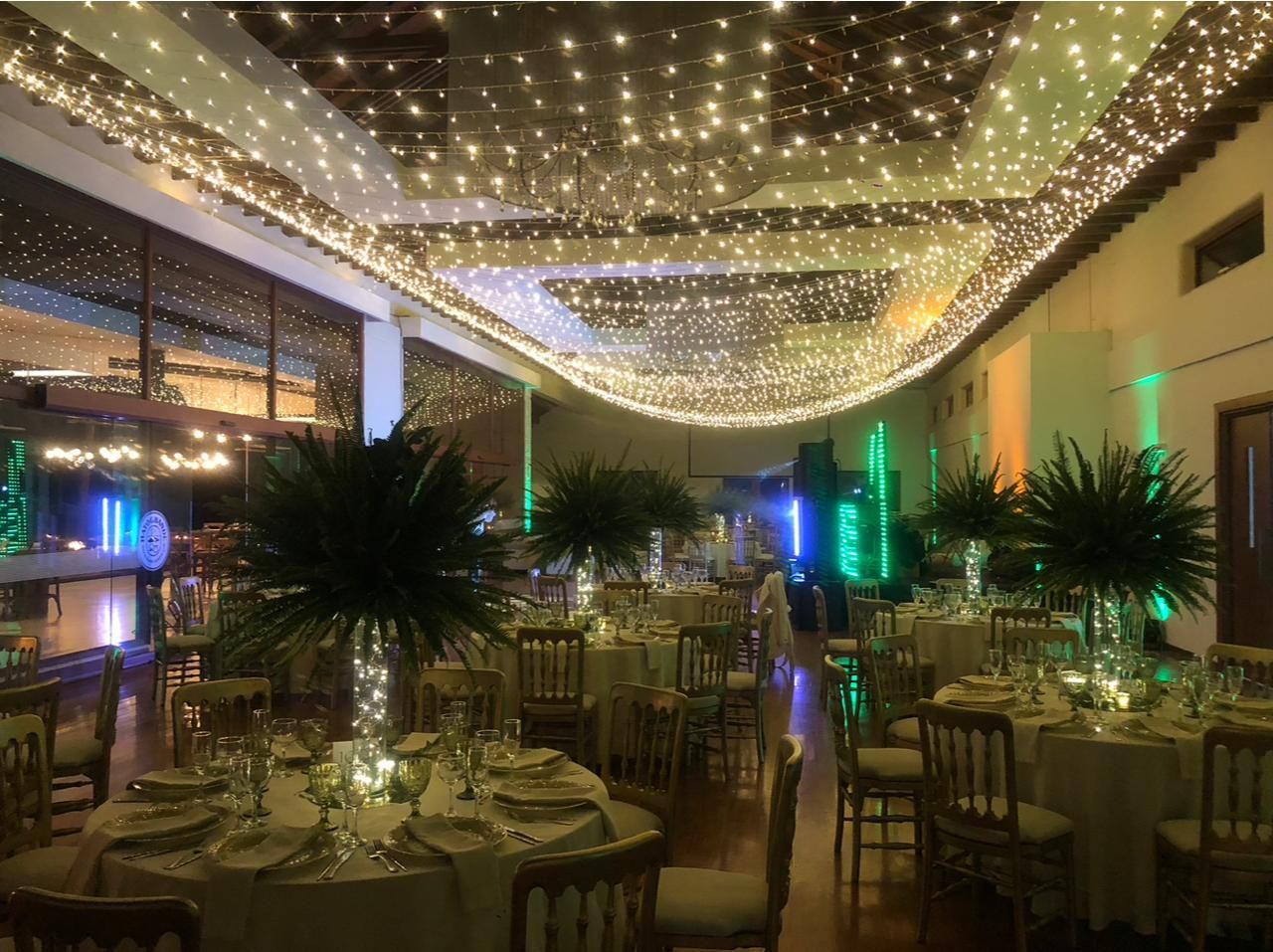 Salón de gala con mesas redondas, centros de mesa de palmas y luces