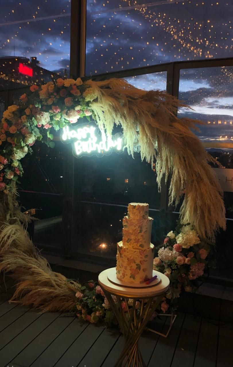 Arco de flores y pampas con letrero de neón de feliz cumpleaños y torta dorada